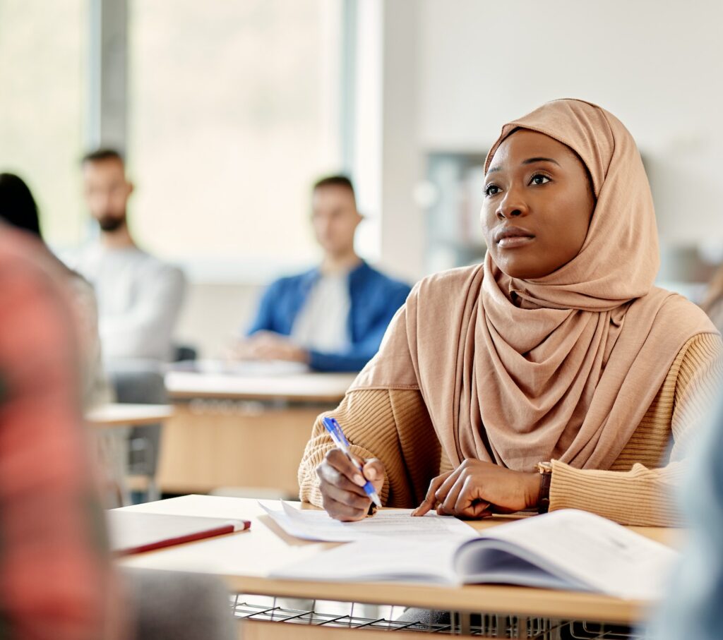 Young black student in hijab attending a class at university classroom.